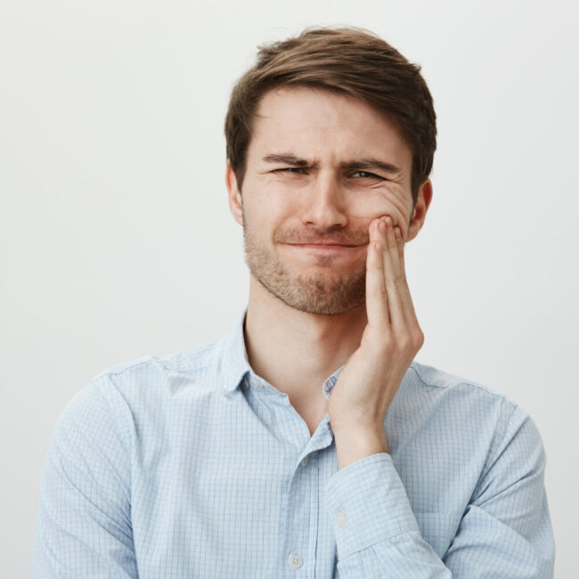 homem-tocando-a-bochecha-e-fazendo-careta-de-dor-de-dente
